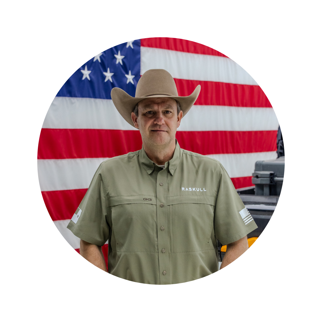 Man wearing a cowboy hat and a shirt with 'Raskull' branding in front of an American flag.