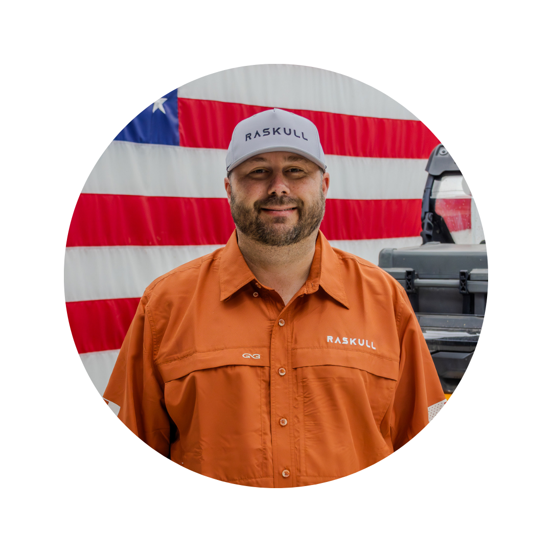 Man wearing an orange Raskull shirt and white cap in front of an American flag